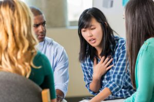Asian woman speaking during a group therapy session while her peers listen.