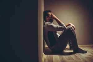 Young depressed man sitting on floor holding his hand to his face in a dark room.