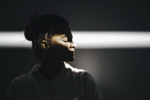 Woman with her eyes closed in a dark room, a small ray of light showing her face.