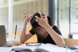 Frustrated woman with ADHD clutches her hands in the air while trying to do her homework.